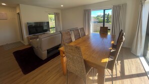 Un salon moderne avec une grande table à manger en bois, des sièges confortables, un téléviseur à écran plat et de grandes fenêtres dotées de rideaux.
