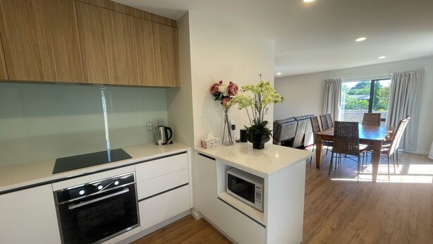 Une cuisine moderne avec des meubles en bois, un four encastré, un four à micro-ondes et un coin repas avec des chaises et une table en osier.
