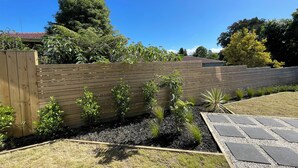 Un jardin avec une clôture en bois, diverses plantes et un chemin pavé.