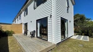 Une maison à deux étages dotée d’une terrasse en bois, de grandes portes-fenêtres coulissantes et d’une cour arrière clôturée.