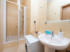 Enjoy a refreshing shower in this bathroom with a walk-in shower, washing machine, and sink with a convenient glass shelf.