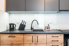 A modern kitchen with a black countertop, a Bosch kettle, a knife block, a sink with a modern faucet, and wooden cabinets. - Raciborska 2-Bedroom Apartment (Katowice)