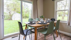 Un coin repas avec une table dressée pour six personnes, entourée de chaises, de grandes fenêtres et offrant une vue sur le jardin.