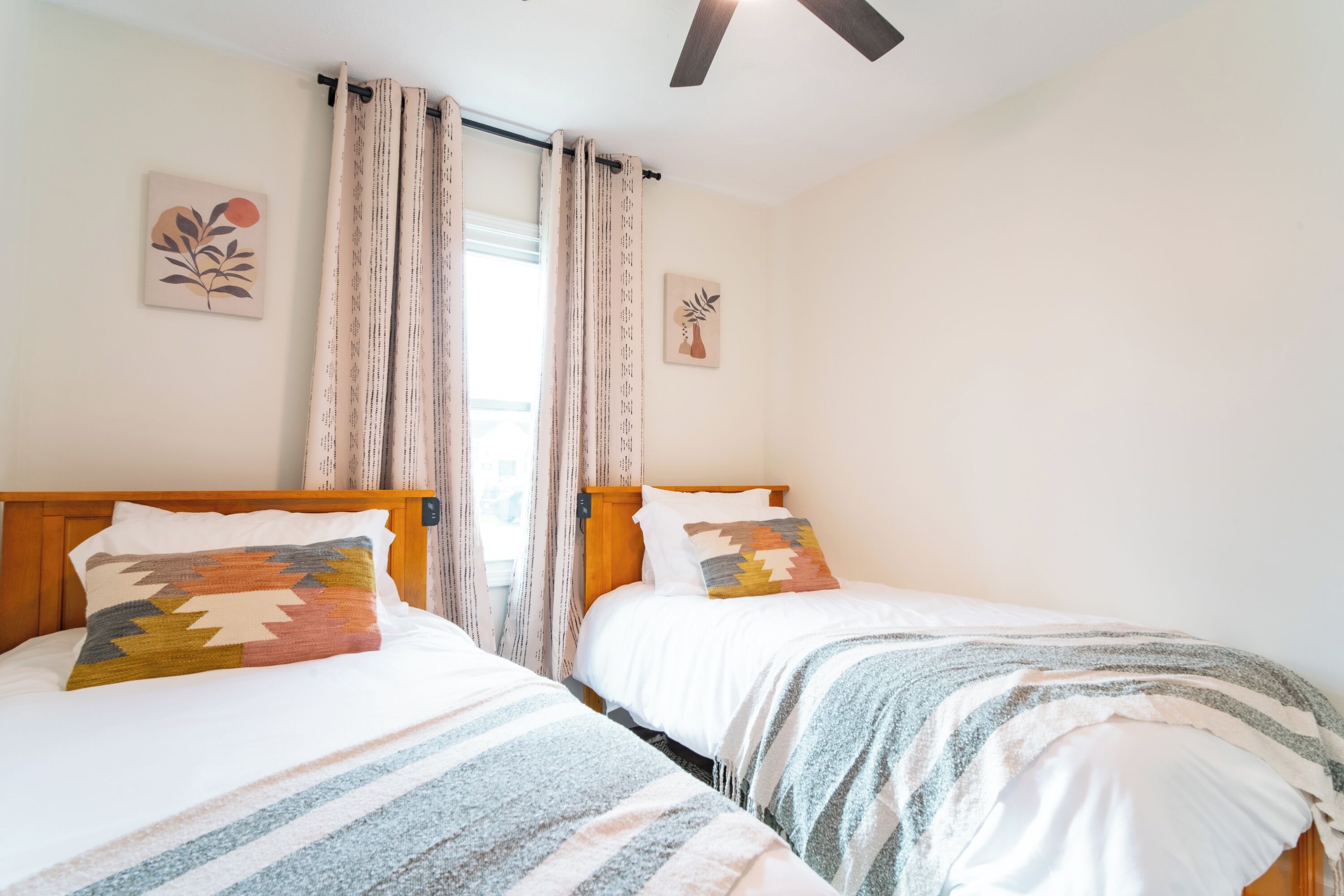 A room with two beds, each with a different patterned blanket and pillow, a wooden headboard, and a ceiling fan.