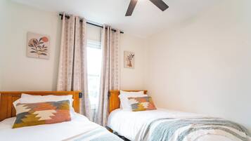 A room with two beds, each with a different patterned blanket and pillow, a wooden headboard, and a ceiling fan.