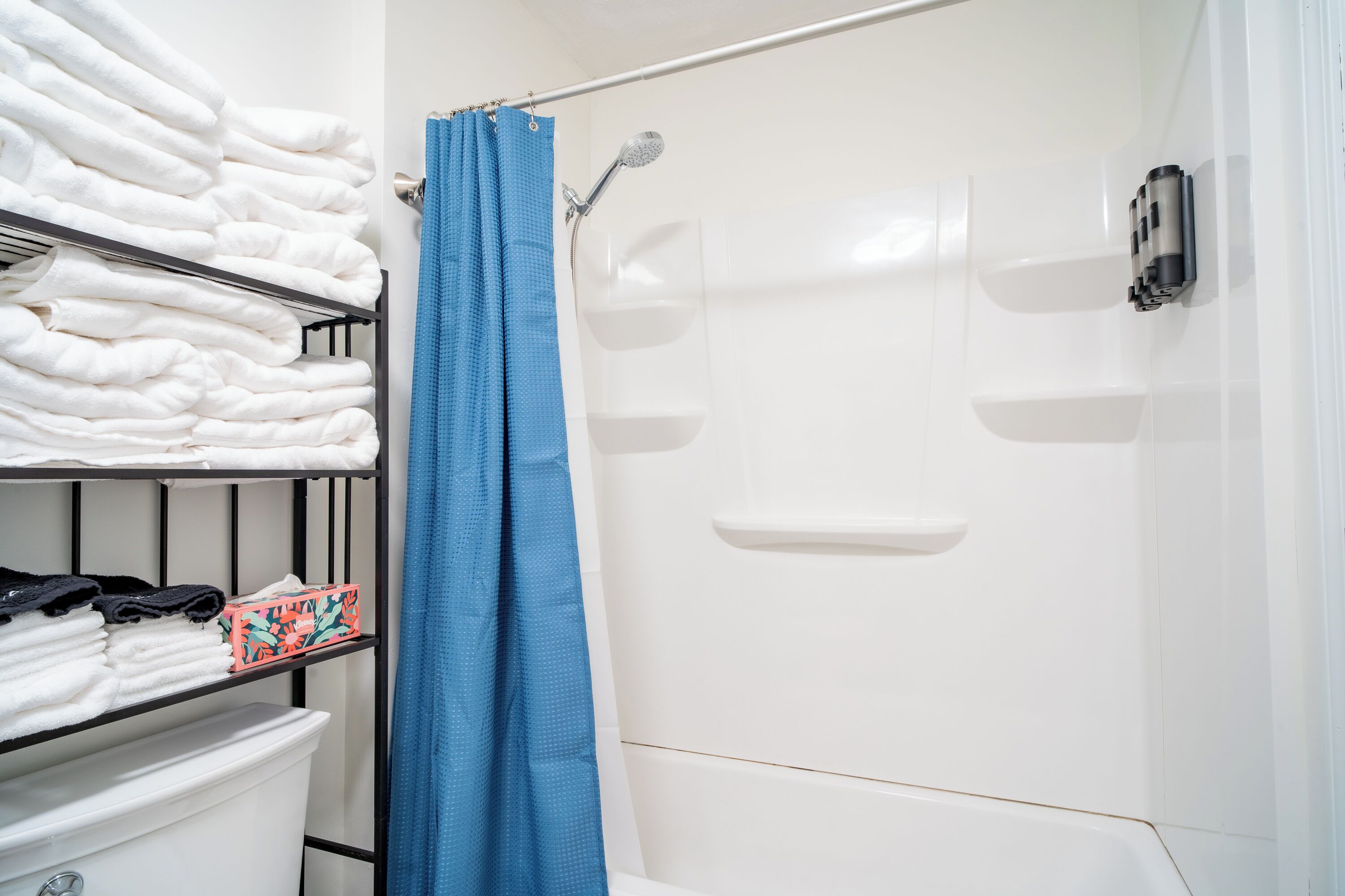 A bathroom with a shower, a shelf with folded towels, and a toilet.