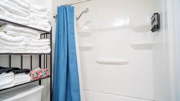 A bathroom with a shower, a shelf with folded towels, and a toilet.