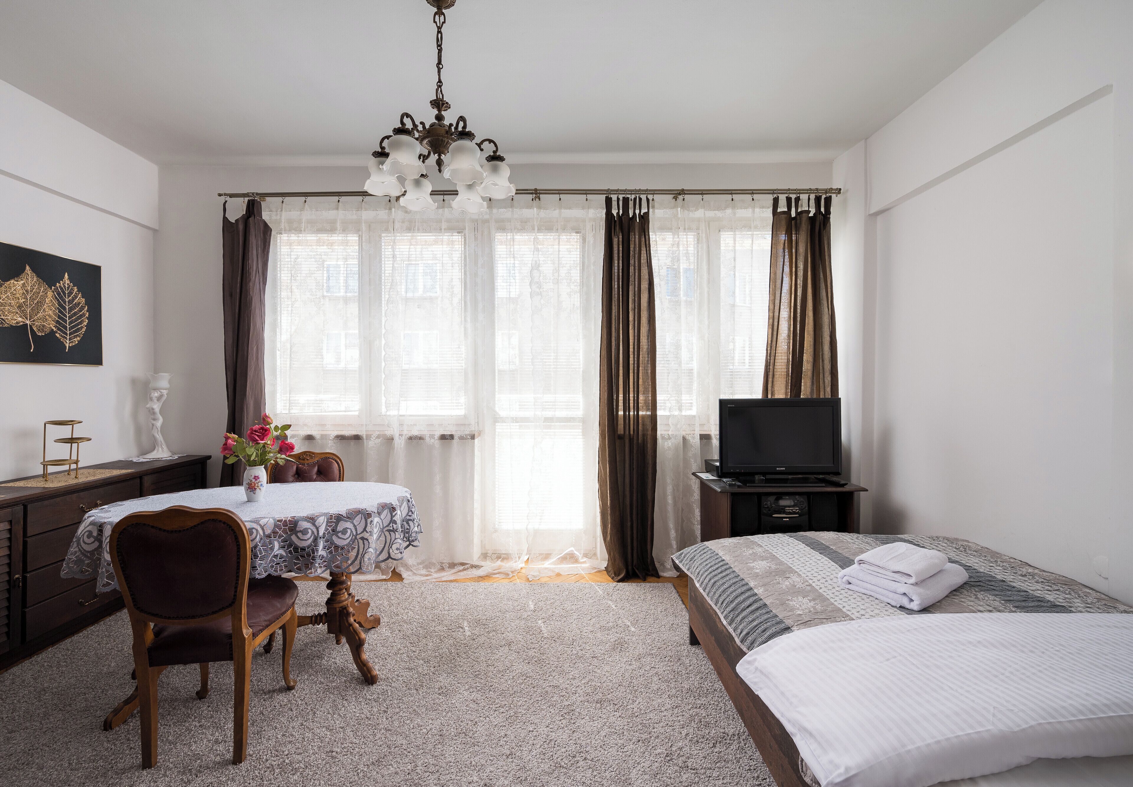 A bedroom with a bed, a TV, a desk with a chair, and a window with curtains.