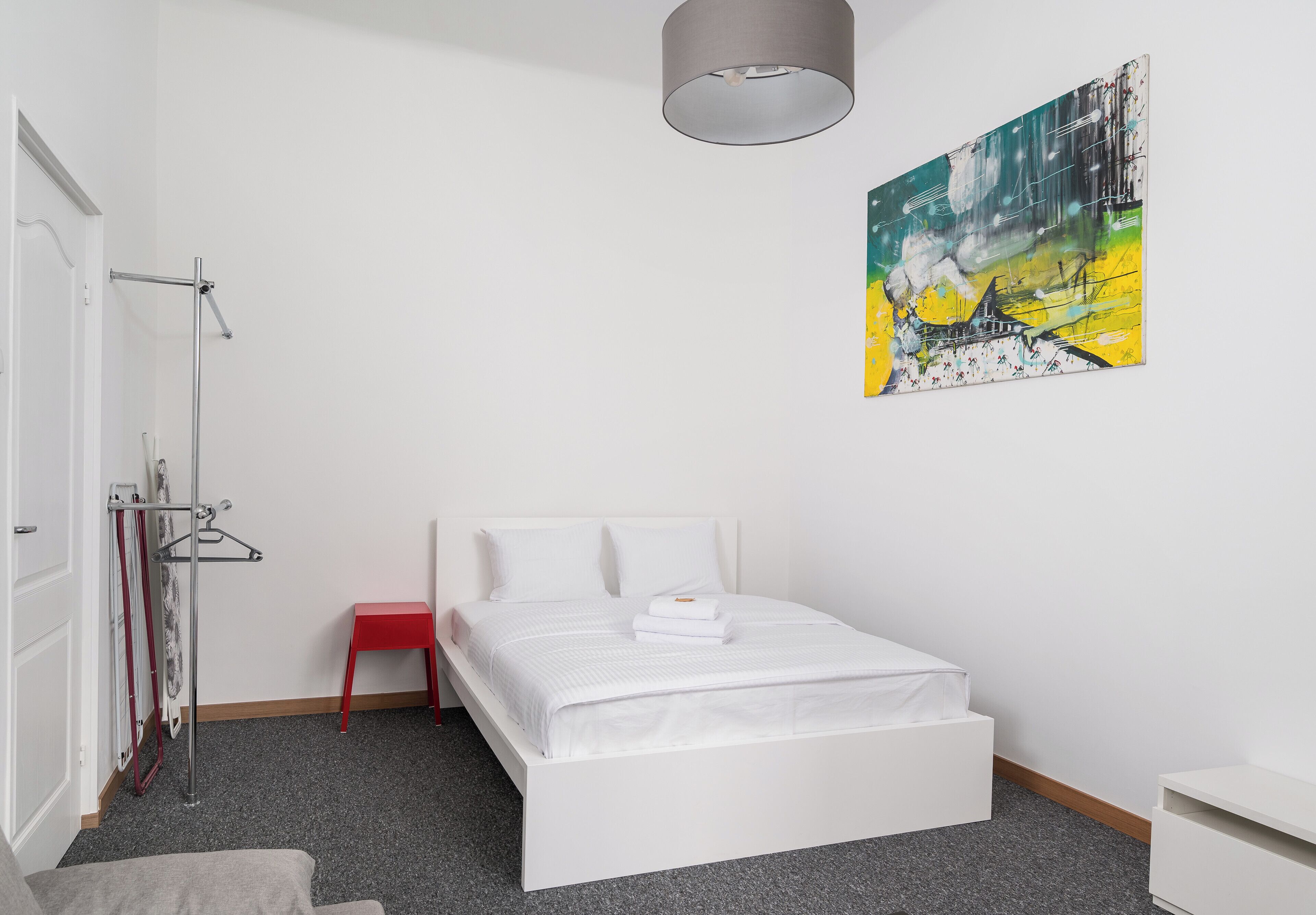 Un dormitorio moderno con una cama blanca, una silla roja, un cuadro en la pared y una lámpara de techo gris.