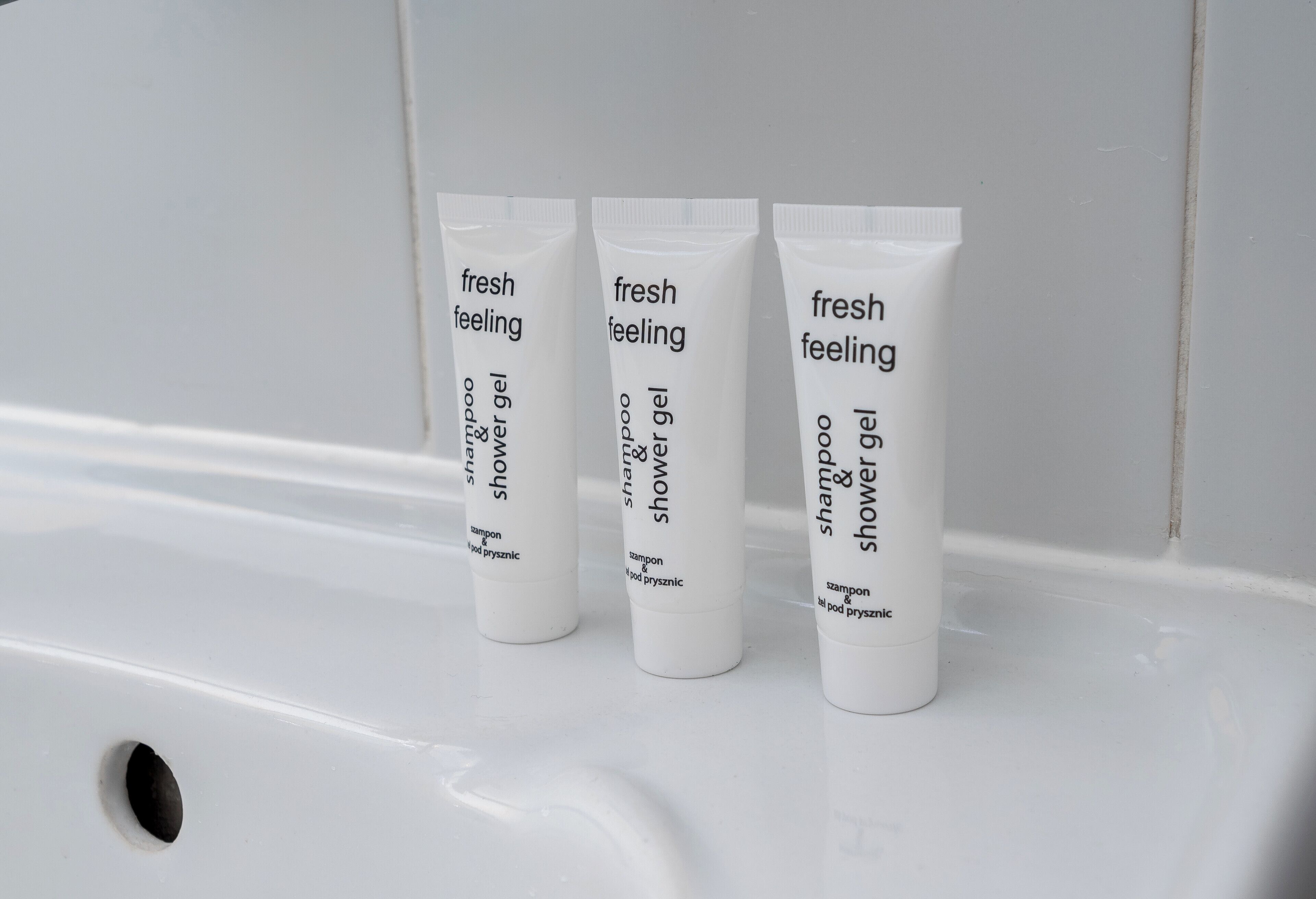 Three tubes of 'fresh feeling' shampoo and shower gel on a white sink.