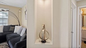 Ett modernt vardagsrum med en soffa i mörk färg, en dekorativ metallskulptur och en infälld taklampa.