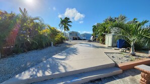A residential street with houses, a driveway, and a gravel path. - Seabreeze Escape WF RV Lot 489 (Cudjoe Key)