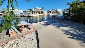 A marina with waterfront properties, including a docked boat and a small dock with a table and chairs. - Seabreeze Escape WF RV Lot 489 (Cudjoe Key)