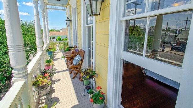 A covered porch with a wooden deck, white railings, and potted plants. - Historic Victorian in New Orleans, minutes from tourist attractions (New Orleans)