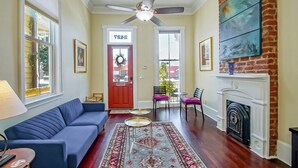 A living room with a blue sofa, a fireplace, a ceiling fan, and a red door with a wreath. - Historic Victorian in New Orleans, minutes from tourist attractions (New Orleans)