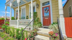 A yellow house with a red door, white columns, and a porch with potted plants. - Historic Victorian in New Orleans, minutes from tourist attractions (New Orleans)