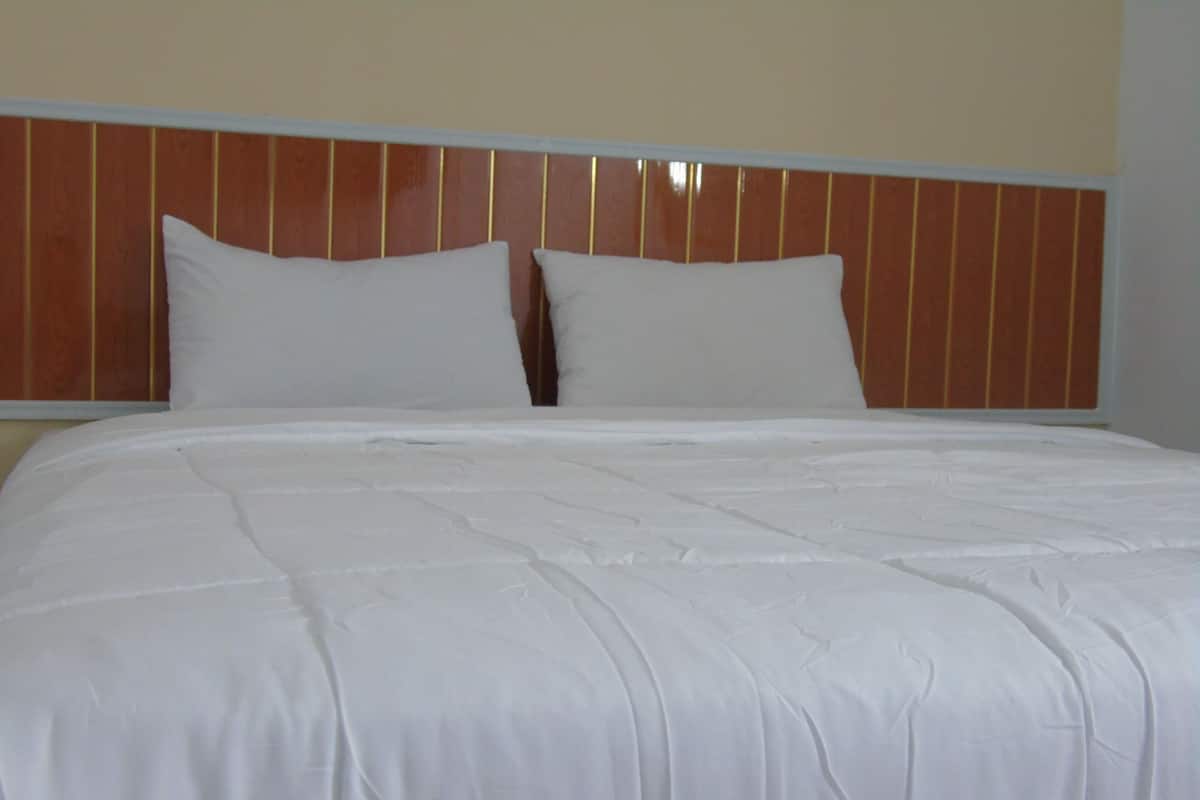 A neatly made bed with white linens and a wooden headboard.