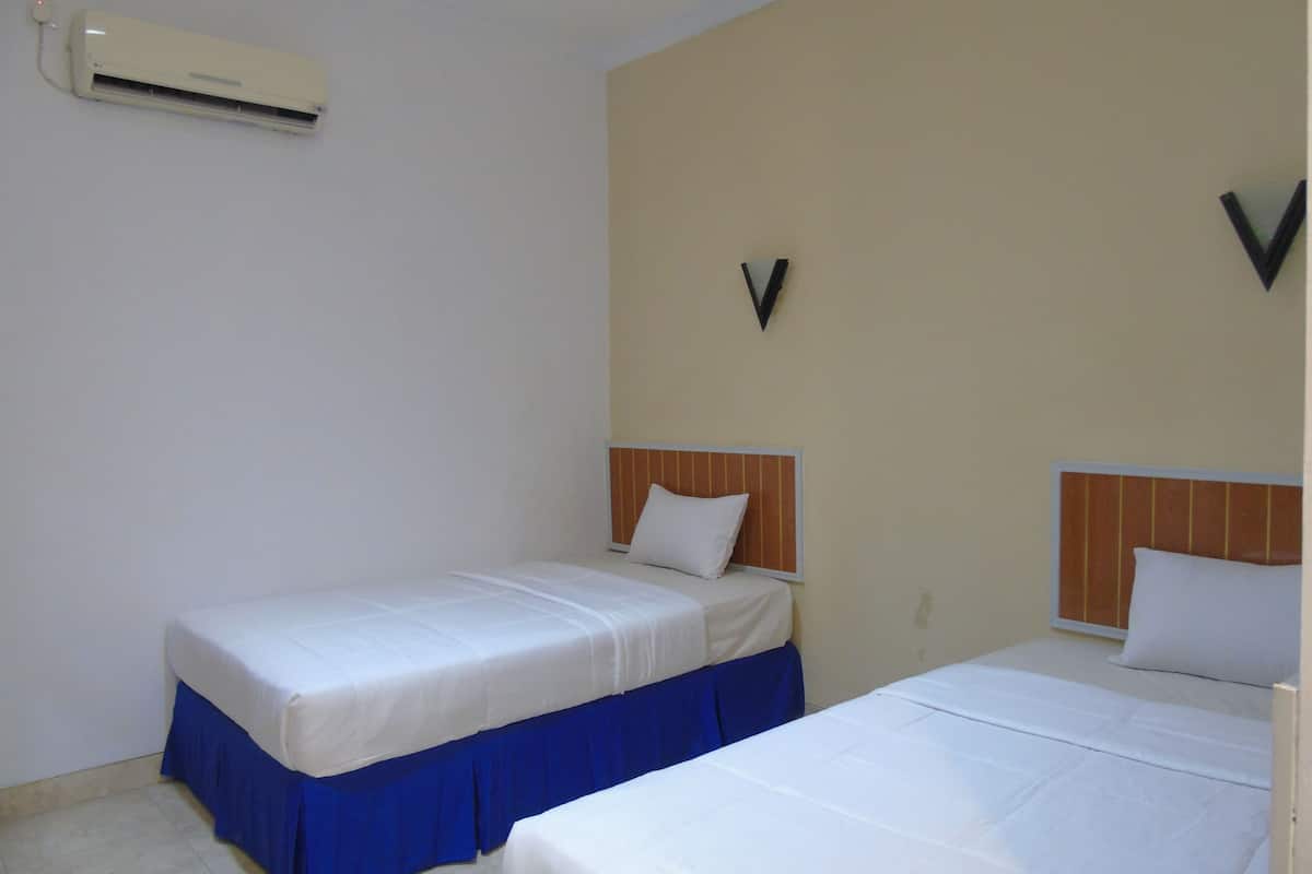 A hotel room with two beds, each with a wooden headboard and white bedding. An air conditioning unit is mounted on the wall.