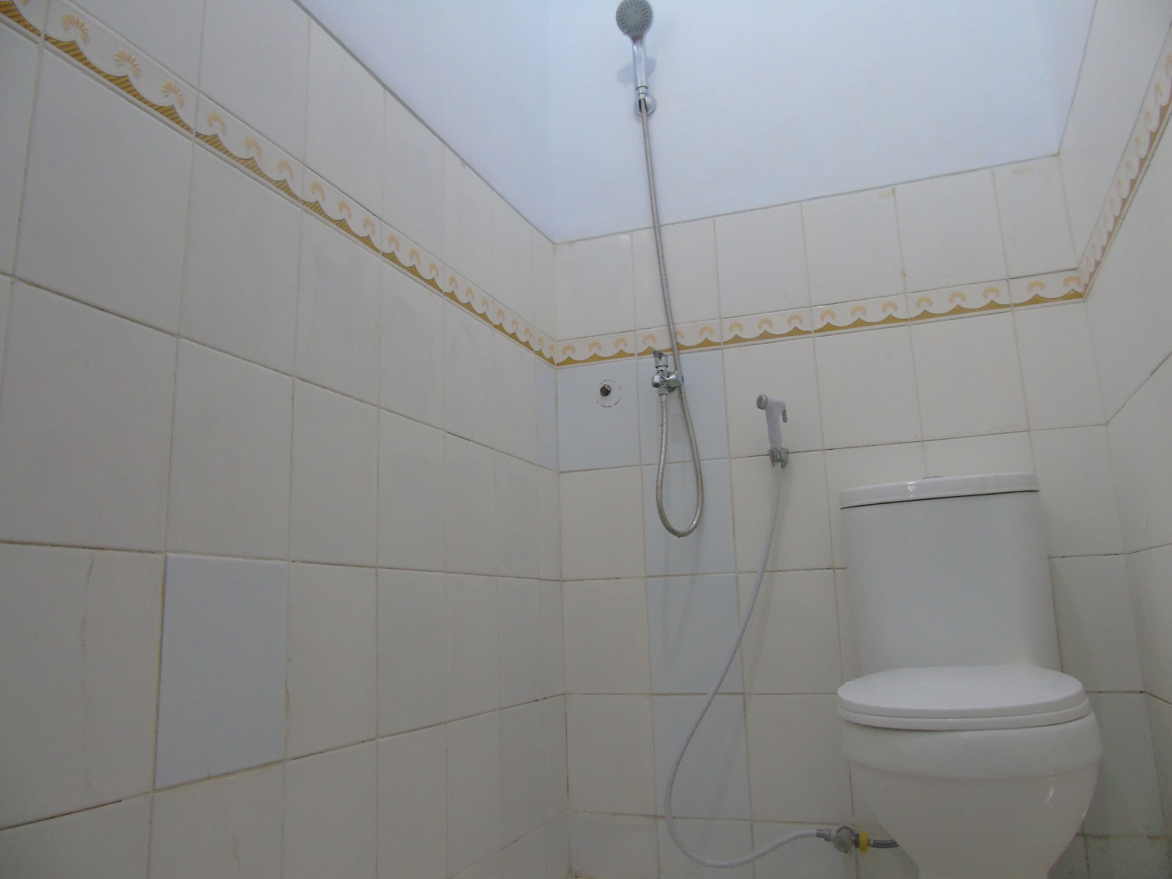 A small, tiled bathroom with a shower, toilet, and a corner sink.