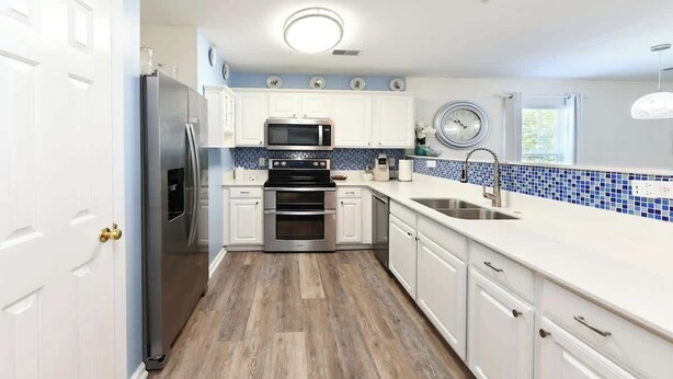 A modern kitchen with white cabinets, a stainless steel refrigerator, a microwave, an oven, and a sink. - Green Fairways Retreat Condo (Myrtle Beach)