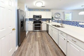 A modern kitchen with white cabinets, a stainless steel refrigerator, a microwave, an oven, and a sink. - Green Fairways Retreat Condo (Myrtle Beach)
