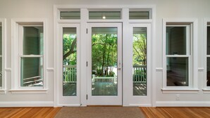 Una habitación con suelo de madera, paredes blancas y una puerta de vidrio que da a una terraza al aire libre.