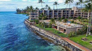 Un hôtel à plusieurs étages doté de balcons donnant sur l’océan, d’un espace piscine et d’un aménagement paysager luxuriant.