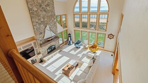 A spacious living area with a stone fireplace, large windows offering a view of the beach, and a cozy seating arrangement. - Stunning Luxury Home on the Sandy Beach Shores of Lake Michigan!! (Sturgeon Bay)