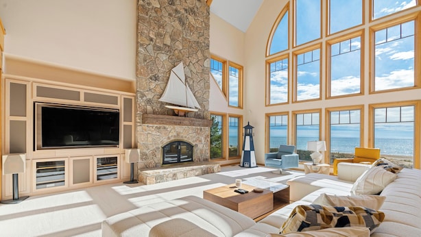 A spacious living room with a stone fireplace, large windows, and a view of the sea. - Stunning Luxury Home on the Sandy Beach Shores of Lake Michigan!! (Sturgeon Bay)