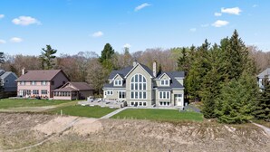 A large, two-story house with a spacious front yard and a sandy area in the foreground. - Stunning Luxury Home on the Sandy Beach Shores of Lake Michigan!! (Sturgeon Bay)