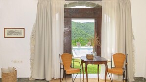 Ein Zimmer mit Blick auf Pool und Berge. Zwei Korbstühle und ein Tisch mit einer Vase sind vorhanden.