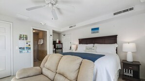 A bedroom with a bed, a nightstand, a chair, a ceiling fan, and a door.