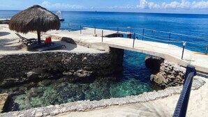 A stone bridge over clear water, a thatched umbrella, and a sandy beach area.