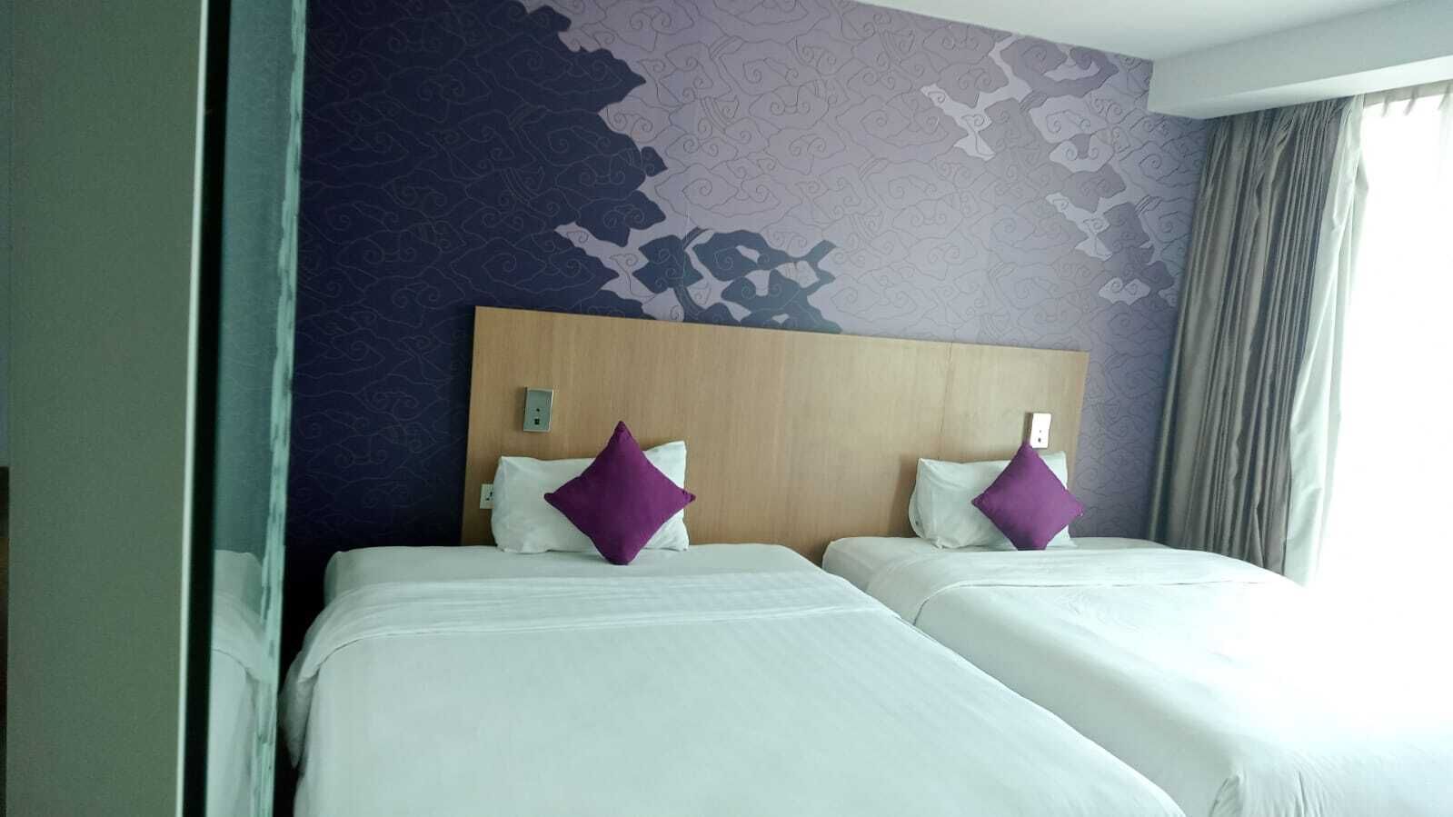 A hotel room with two beds, purple pillows, a wooden headboard, and a patterned wall.