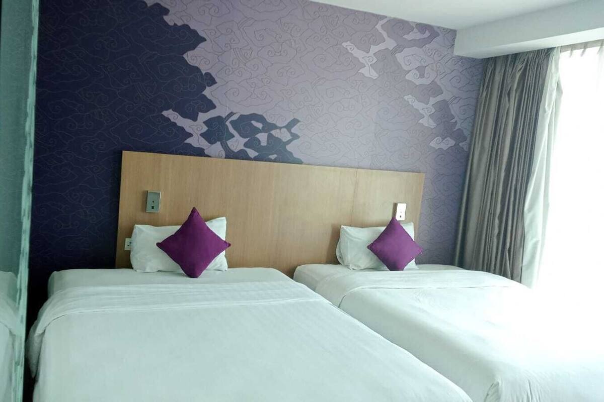 A hotel room with two beds, purple pillows, a wooden headboard, and a patterned wall.
