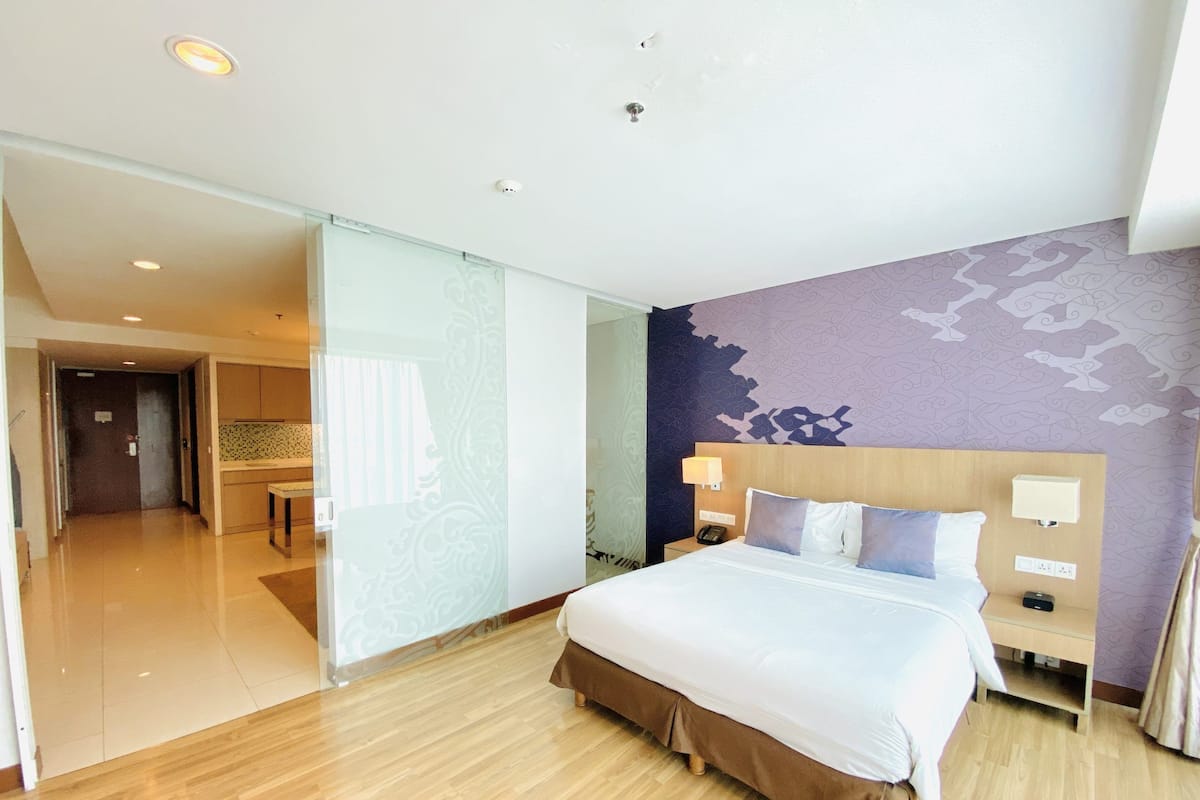 A hotel room with a large bed, a bedside table with a lamp, a phone, and a wall with a floral pattern.