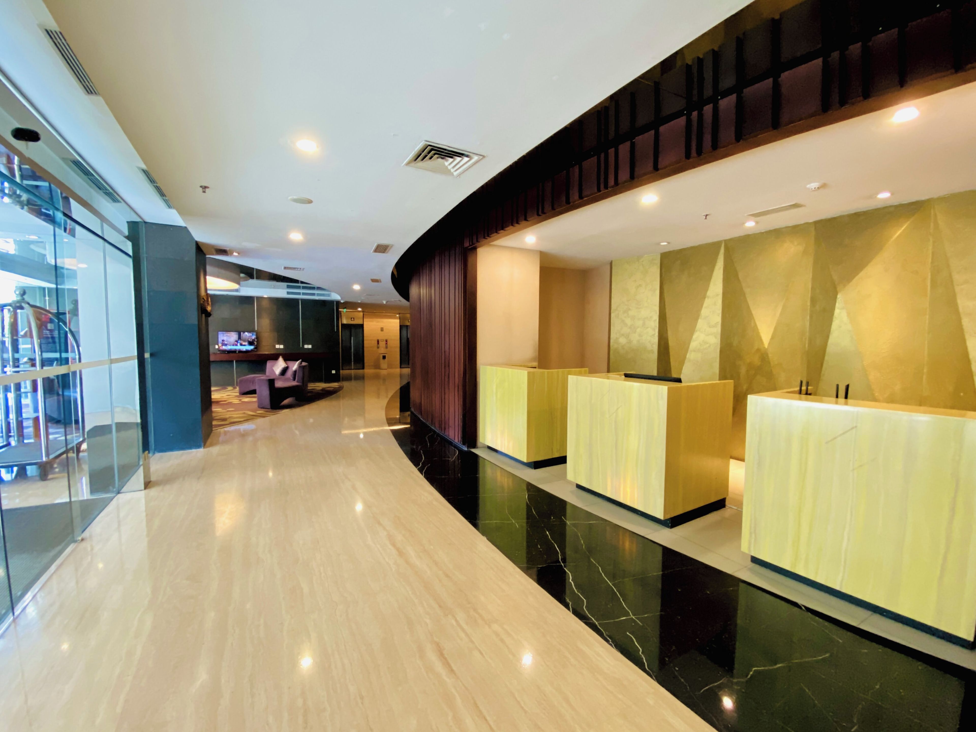 Een moderne hotellobby met een gebogen receptiebalie, een zithoek met een bank, en een glazen wand aan de ene kant.