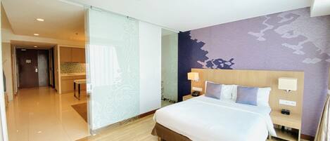 A hotel room with a large bed, a bedside table with a lamp, a phone, and a wall with a floral pattern.