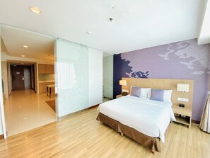 Quarto de hotel com uma cama grande, mesa de cabeceira com abajur, telefone e parede com padrão floral.