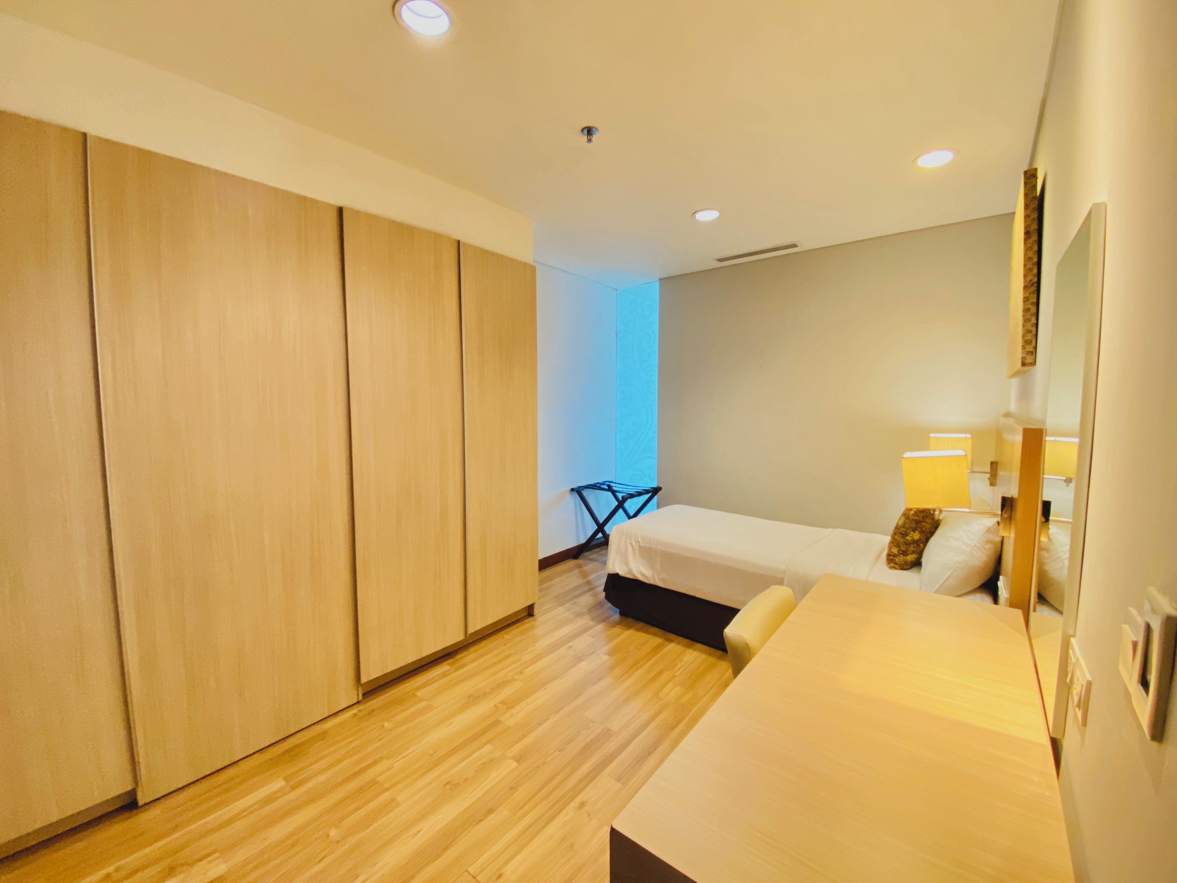 Een moderne slaapkamer met een houten vloer, een bed met kussens, een nachtkastje en een kledingkast.