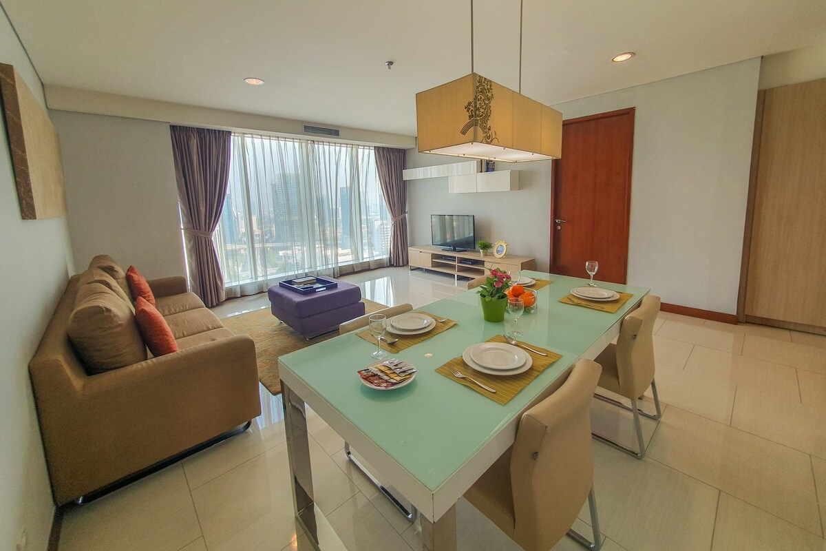 A modern living room with a sofa, a dining table set for two, and a television.