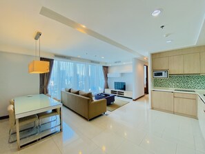 A modern living room with a sofa, TV, and dining area. There is a kitchen with cabinets and a microwave. - Habitare Rasuna Jakarta (Surabaya)
