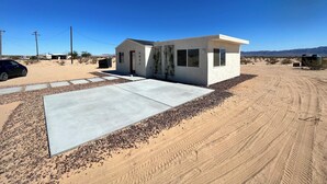 A modern single-story house with a concrete driveway and a desert landscape in the background.