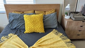 A bed with a wooden headboard, two pillows, a yellow throw blanket, and a desk with a typewriter.