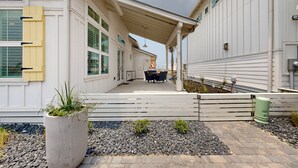Un patio cubierto con una mesa y sillas, una maceta de concreto con plantas y una valla de madera.