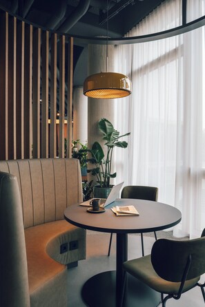 Ein modernes Interieur mit einem runden Tisch, Stühlen, einer Couch, einer Pendelleuchte und einem großen Fenster mit leichtem Vorhang.