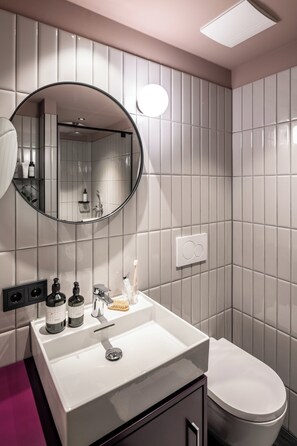 Ein Badezimmer mit einem weißen Waschbecken, einem runden Spiegel und einer Toilette.
