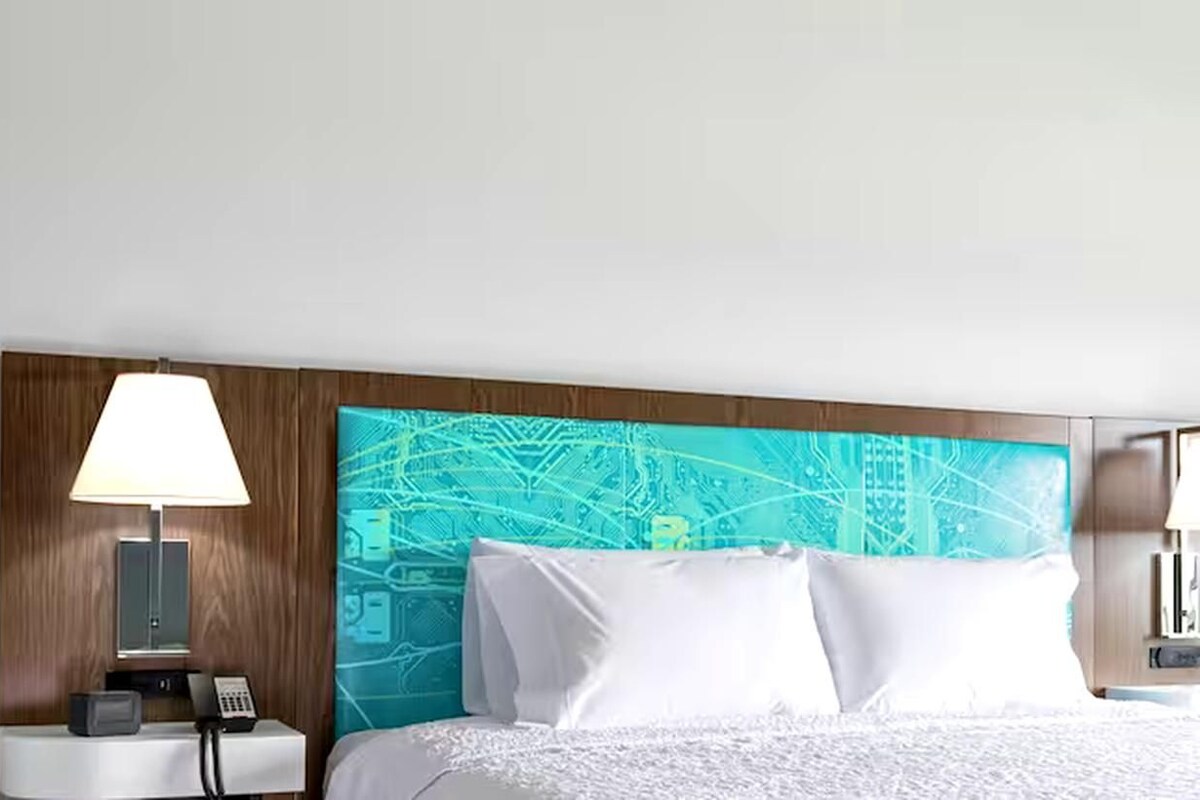 Et hotelværelse med en seng, et natbord med en lampe og en væg med et print af et printkort.