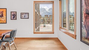 A modern room with a large window, wooden flooring, and framed artwork on the wall. - Spring Creek Vacations 2 BR Premier Condo 203TM (Canmore)