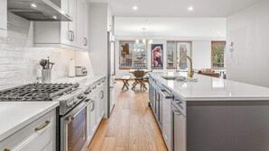 A modern kitchen with white cabinetry, a large island, and a view into the dining area. - Spring Creek Vacations 2 BR Premier Condo 203TM (Canmore)
